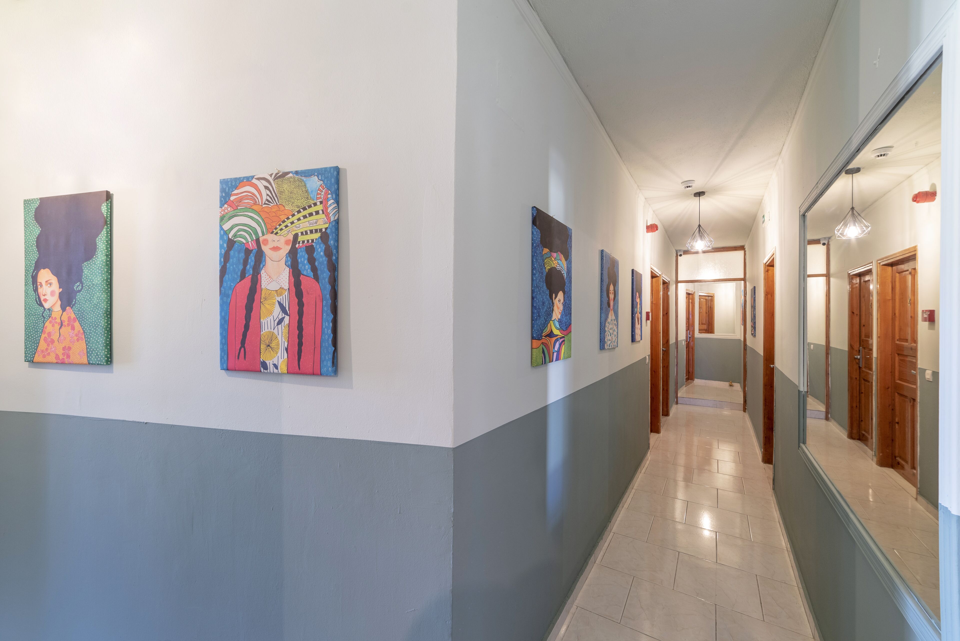 A hallway with artwork on the walls, a tiled floor, and wooden doors.