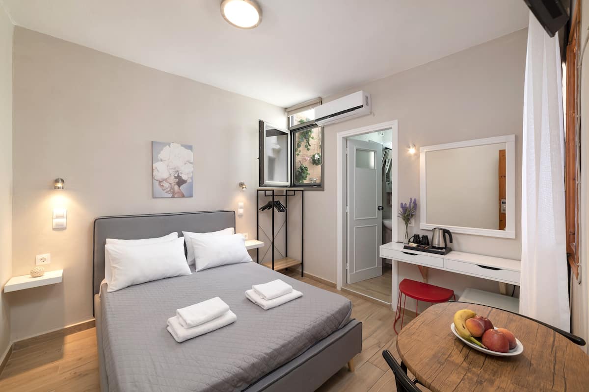 A modern hotel room with a bed, bedside table, desk, and a small dining table with fruit.