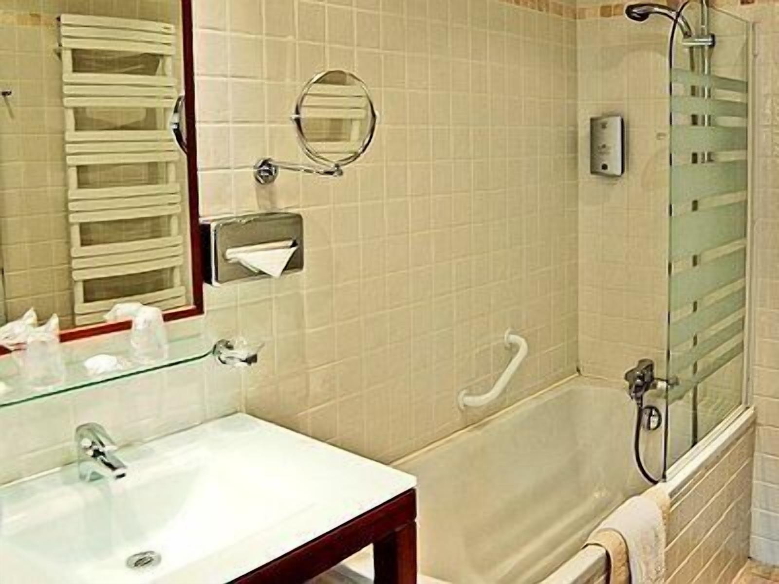 Ein Badezimmer mit weißem Waschbecken, einem Spiegel, einem Handtuchhalter, einer Duschkabine aus Glas und einer Toilette.