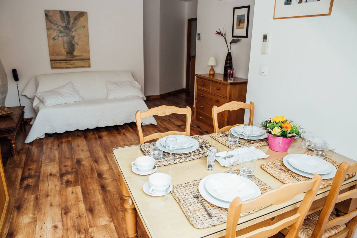 Un comedor ordenado con una mesa de madera dispuesta para cuatro personas, rodeada de sillas de madera.