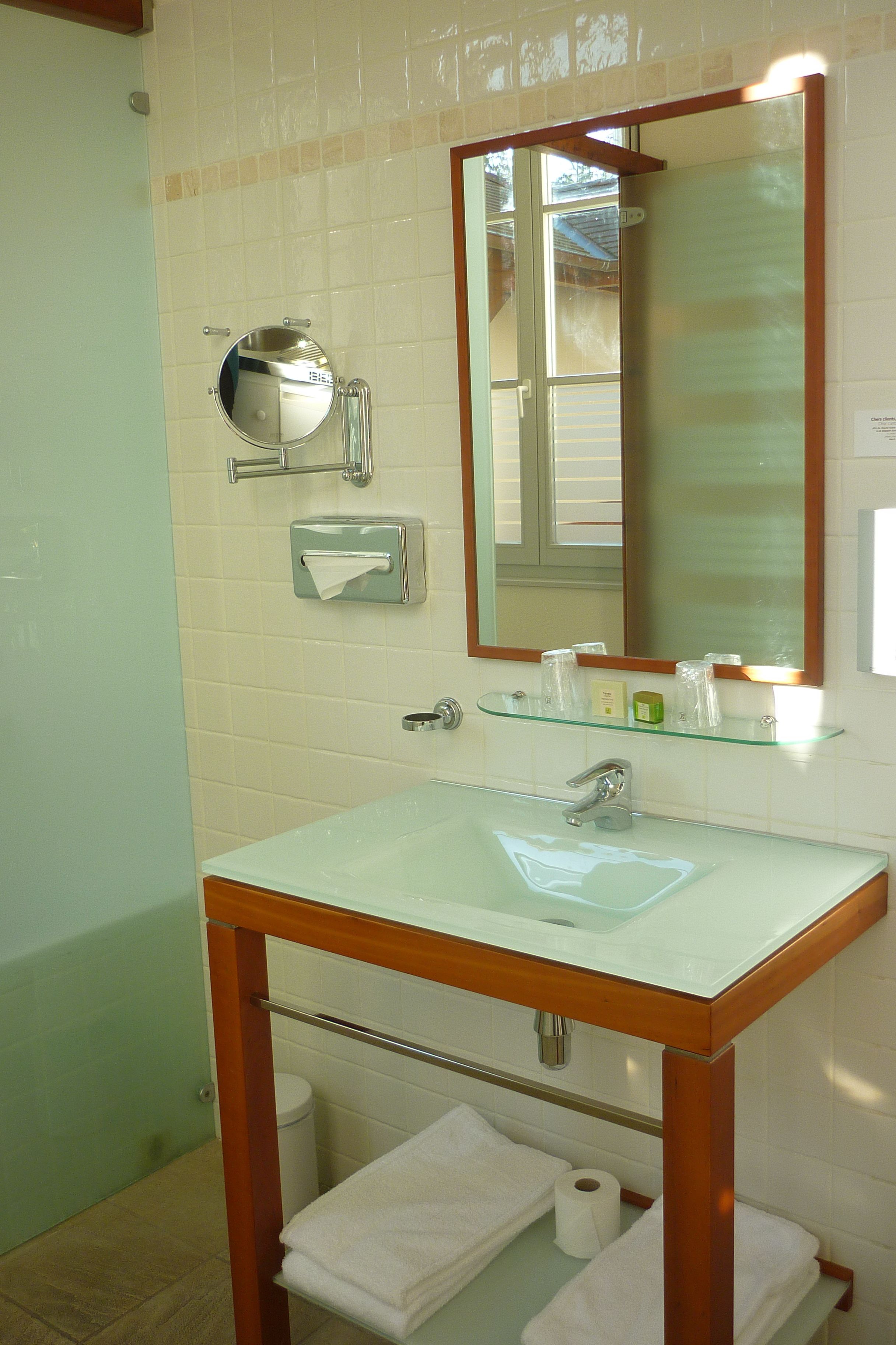 Ein Badezimmer mit einem Glaswaschbecken, einem Spiegel, einem Handtuchhalter und einer Toilette.