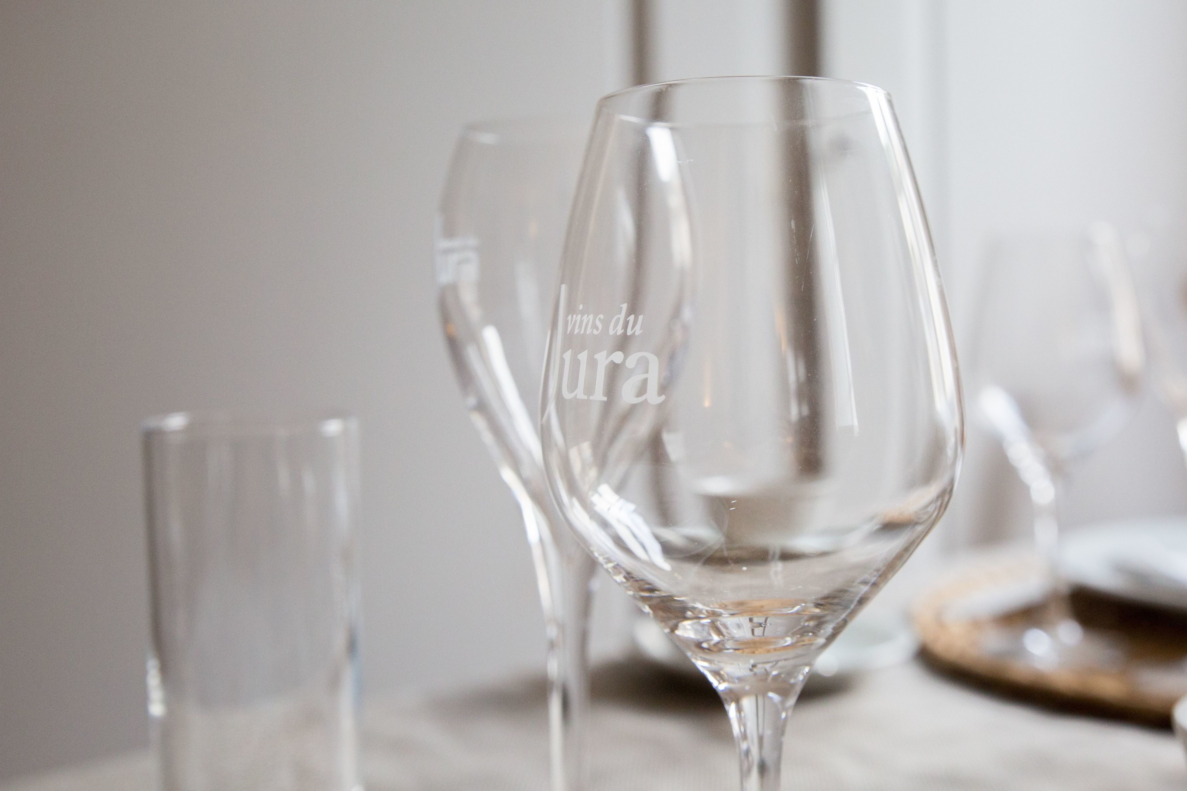 A table with several clear wine glasses, one prominently displaying the inscription "vins du lura."