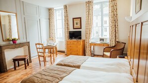 Una habitación de hotel con dos camas, un tocador de madera, un escritorio con una computadora, una silla y un espejo.