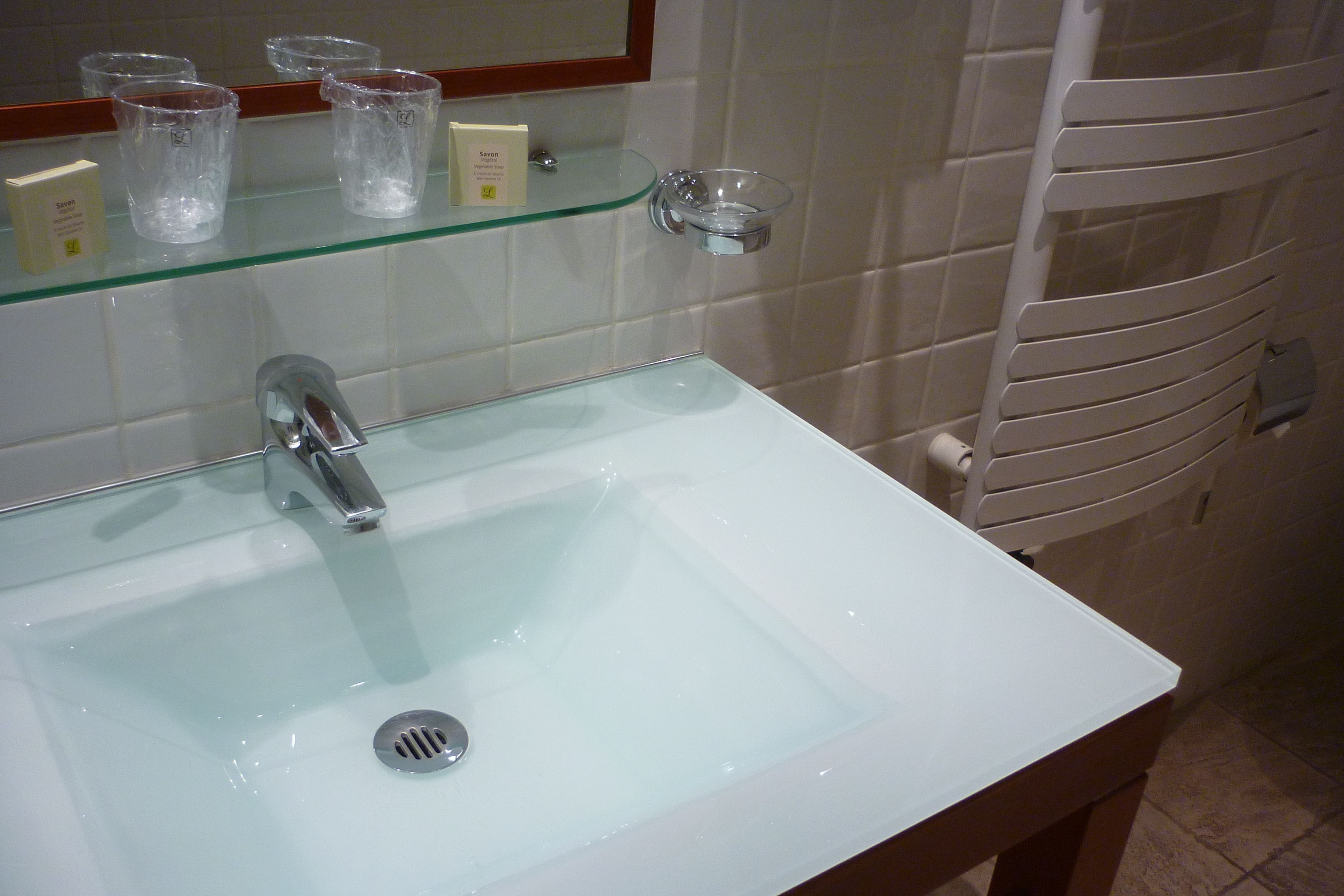 Un baño con un lavamanos blanco, estantes de vidrio y un toallero blanco.