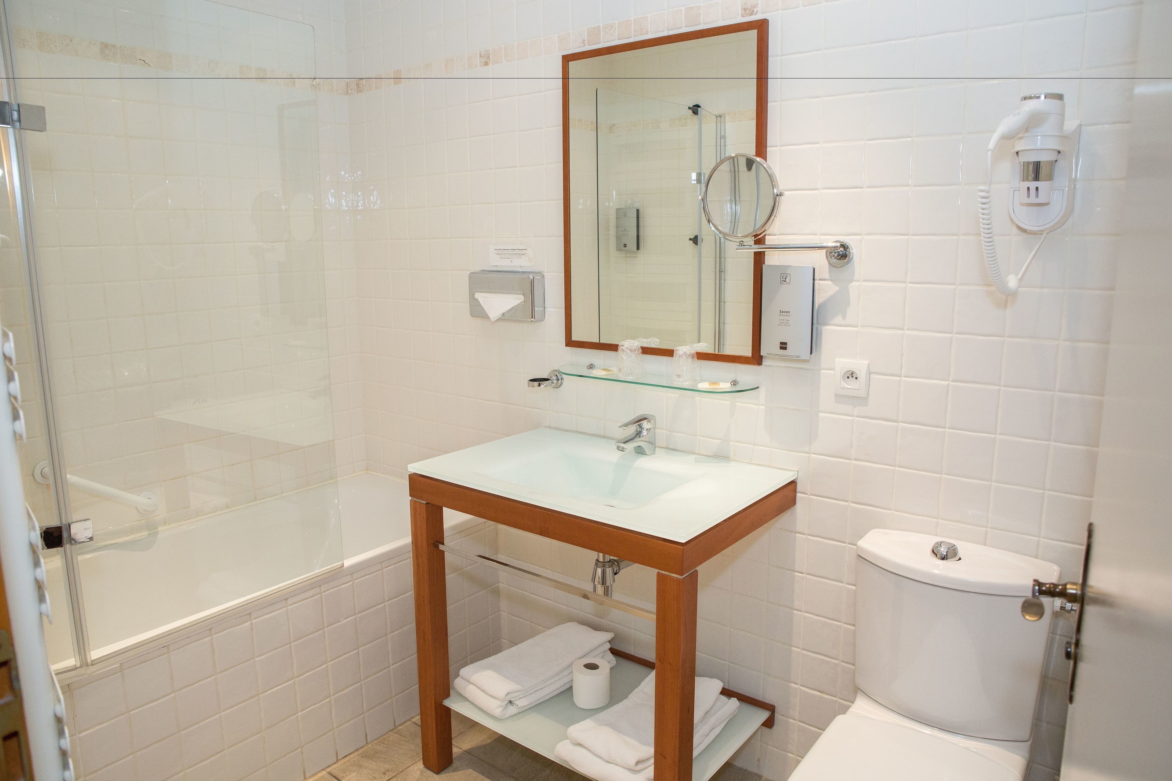 Een badkamer met een douche in een glazen cabine, een wit wastafelmeubel met houten details, en een toilet.
