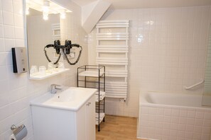 Une salle de bain moderne avec un lavabo blanc, un miroir, un sèche-cheveux et une étagère avec des serviettes.
