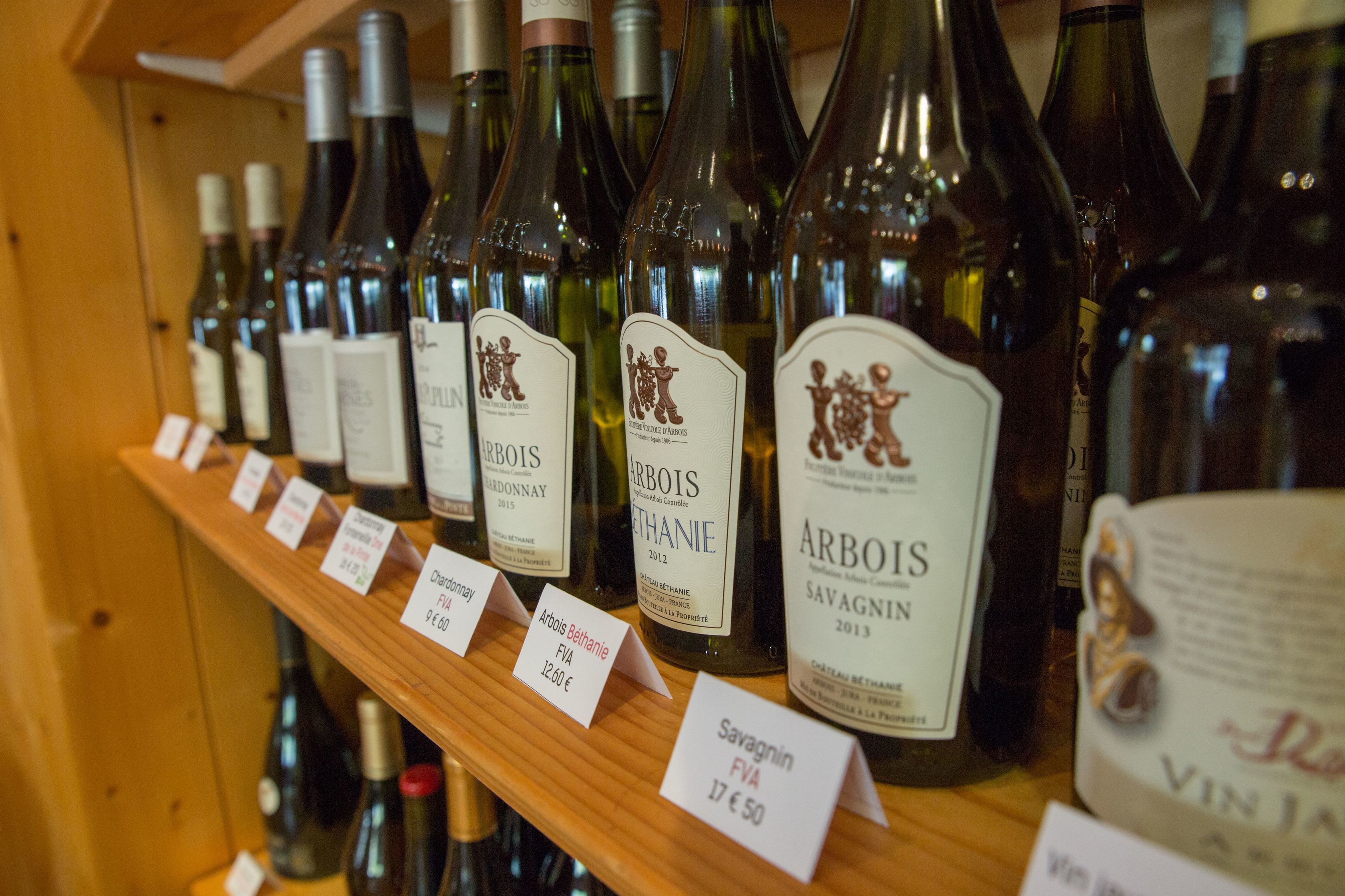 Una estantería con botellas de vino etiquetadas 'Arbois' y 'Savagnin', con precios indicados.