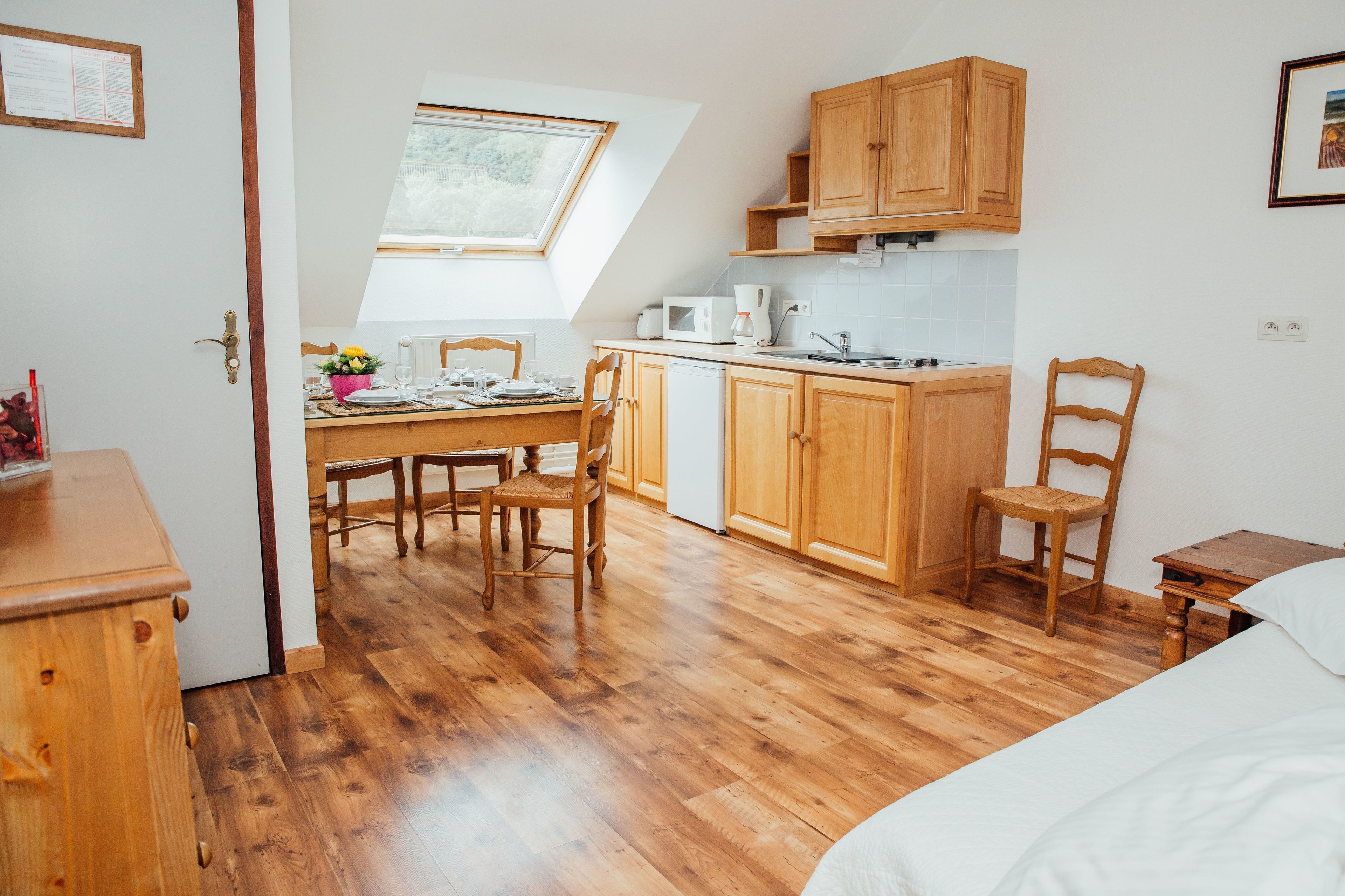 A compact kitchen with wooden cabinets, a dining table with chairs, and a small refrigerator.
