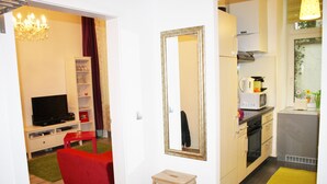 Un espacio habitable pequeño con una televisión, sofá rojo, taburete de madera y una zona de cocina con microondas y hervidor.
