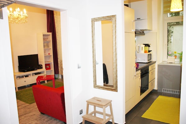 A compact living space with a television, red sofa, wooden stool, and a kitchen area with a microwave and kettle.