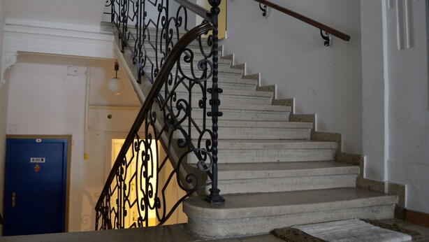 Una escalera con barandillas de metal negro ornamentado y baranda de madera.