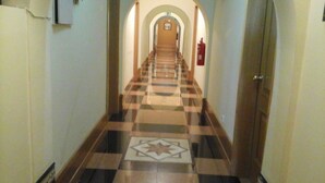 Un couloir au sol carrelé, un extincteur accroché au mur et une porte au fond.