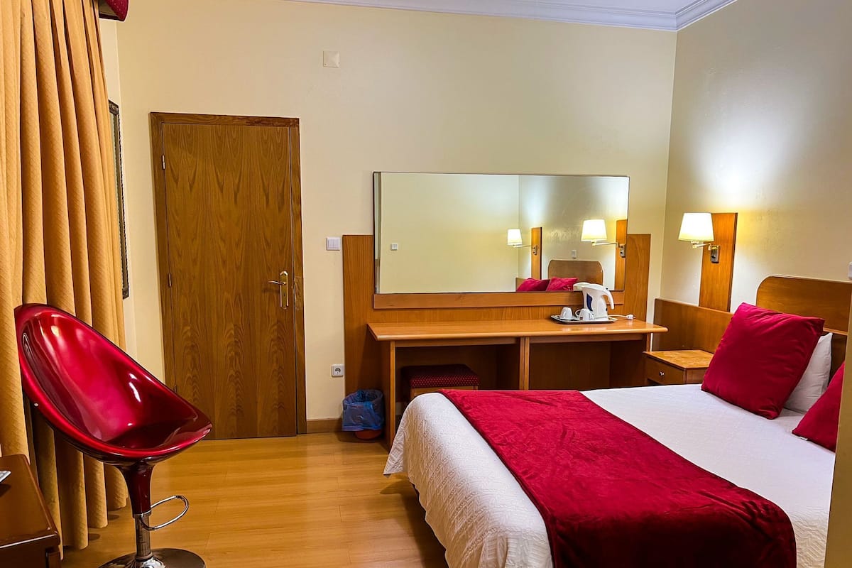 Quarto de hotel com cama, escrivaninha, cadeira e espelho.
