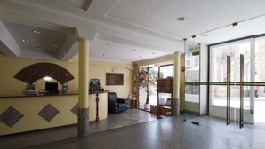 Un hall d’entrée spacieux comprenant un comptoir d’accueil, un espace salon et de grandes fenêtres donnant sur la rue.