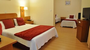 Une chambre d’hôtel avec un grand lit, un lit plus petit, un bureau, une télévision et une lampe.