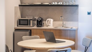 A compact kitchen with a microwave, coffee maker, and kettle, a sink, and a laptop on a round table. - Captain Karas Collection (Paralimni)
