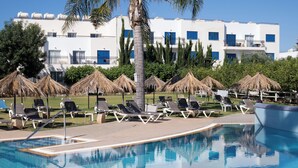 Une piscine entourée de chaises longues, de palmiers et d’un bâtiment blanc agrémenté de touches de bleu.