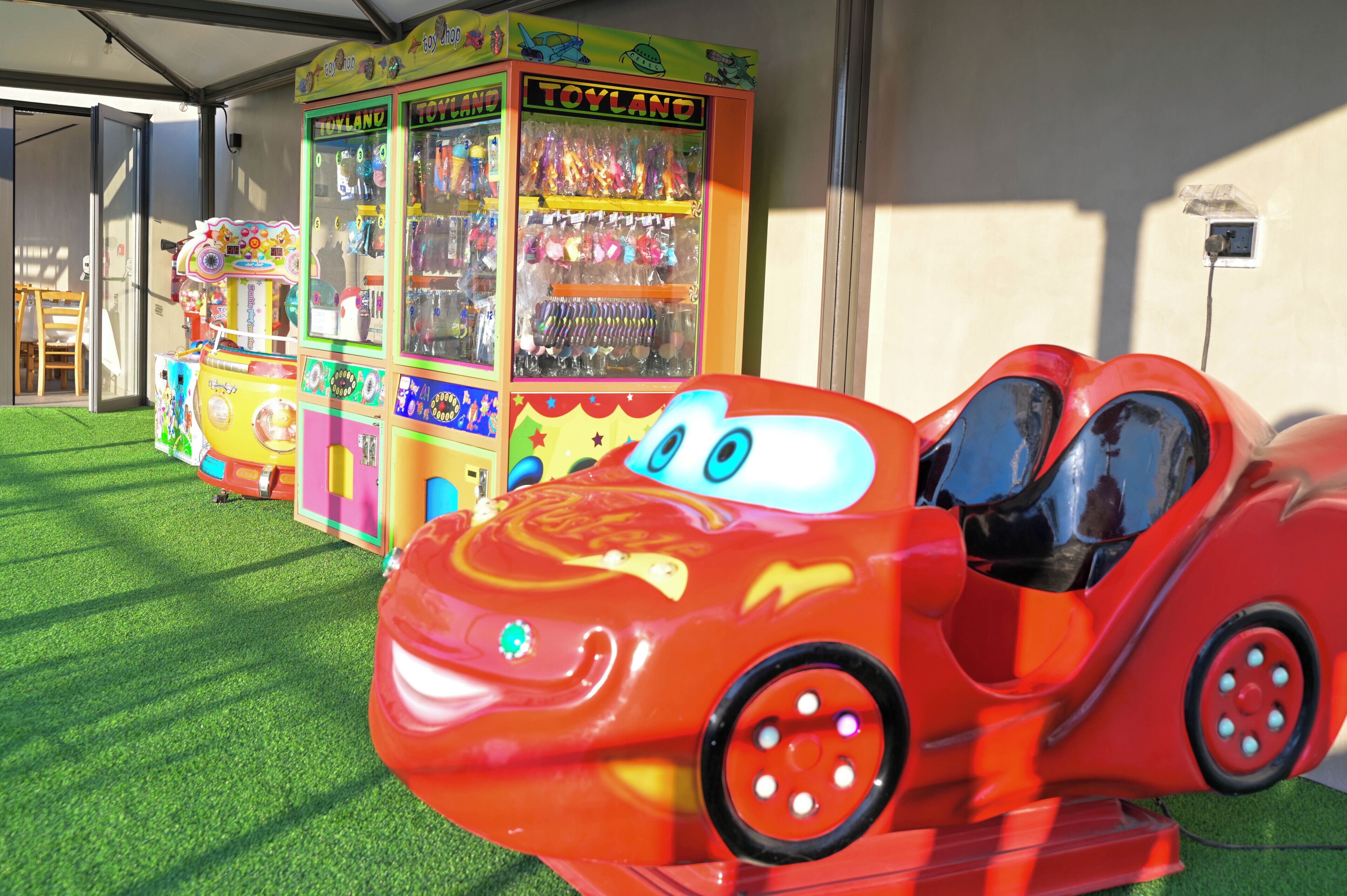 A red toy car ride with a Toyland arcade in the background.