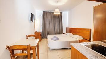 A hotel room with a bed, a desk, a chair, a television, and a kitchenette.