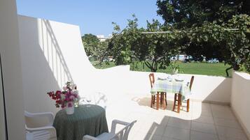 A patio with a table and chairs, a vase of flowers, and a view of a green park.