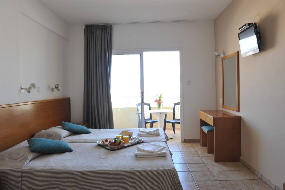 A hotel room with a bed, a desk, a chair, and a balcony with a table and chairs.