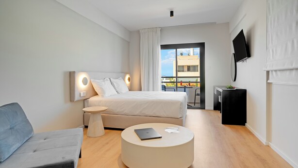 A modern hotel room with a bed, a round coffee table, a sofa, a TV, and a balcony with a view. - Captain Karas Collection (Paralimni)