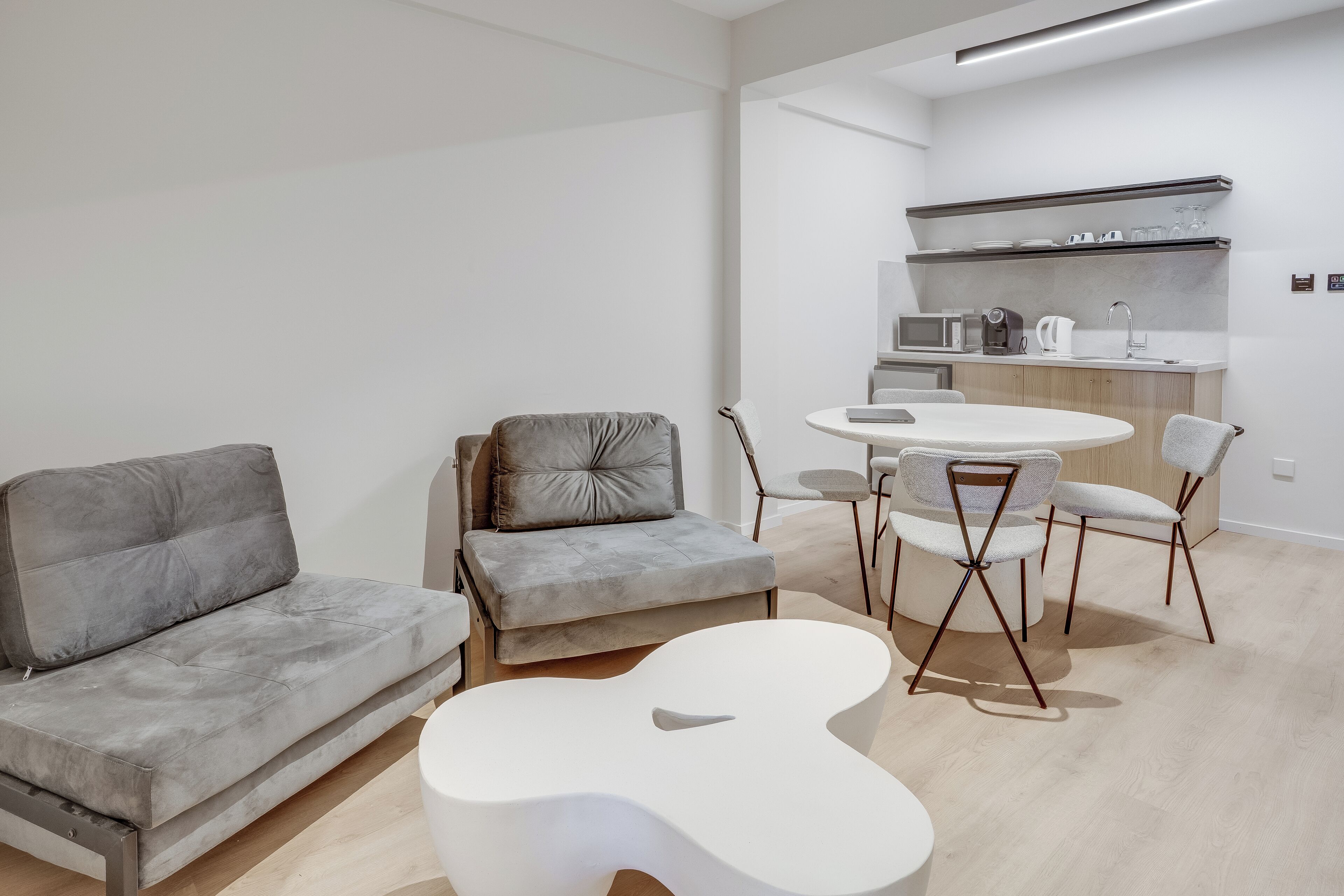 Ein modernes Wohnzimmer mit einem grauen Sofa, einem weißen Couchtisch und einem kleinen Esstisch mit Stühlen.