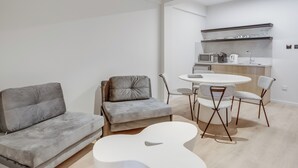 A modern living room with a grey sofa, a white coffee table, and a small dining table with chairs. - Captain Karas Collection (Paralimni)