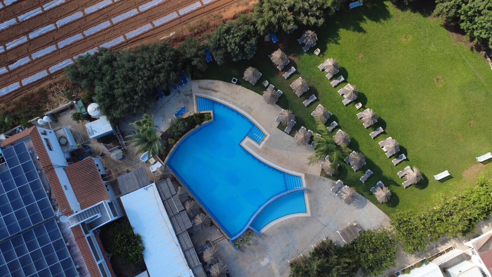 Ein Schwimmbecken, umgeben von Liegestühlen und Sonnenschirmen, mit einer Anlage zur Nutzung von Sonnenenergie und einem Gebäude mit einem Ziegeldach.