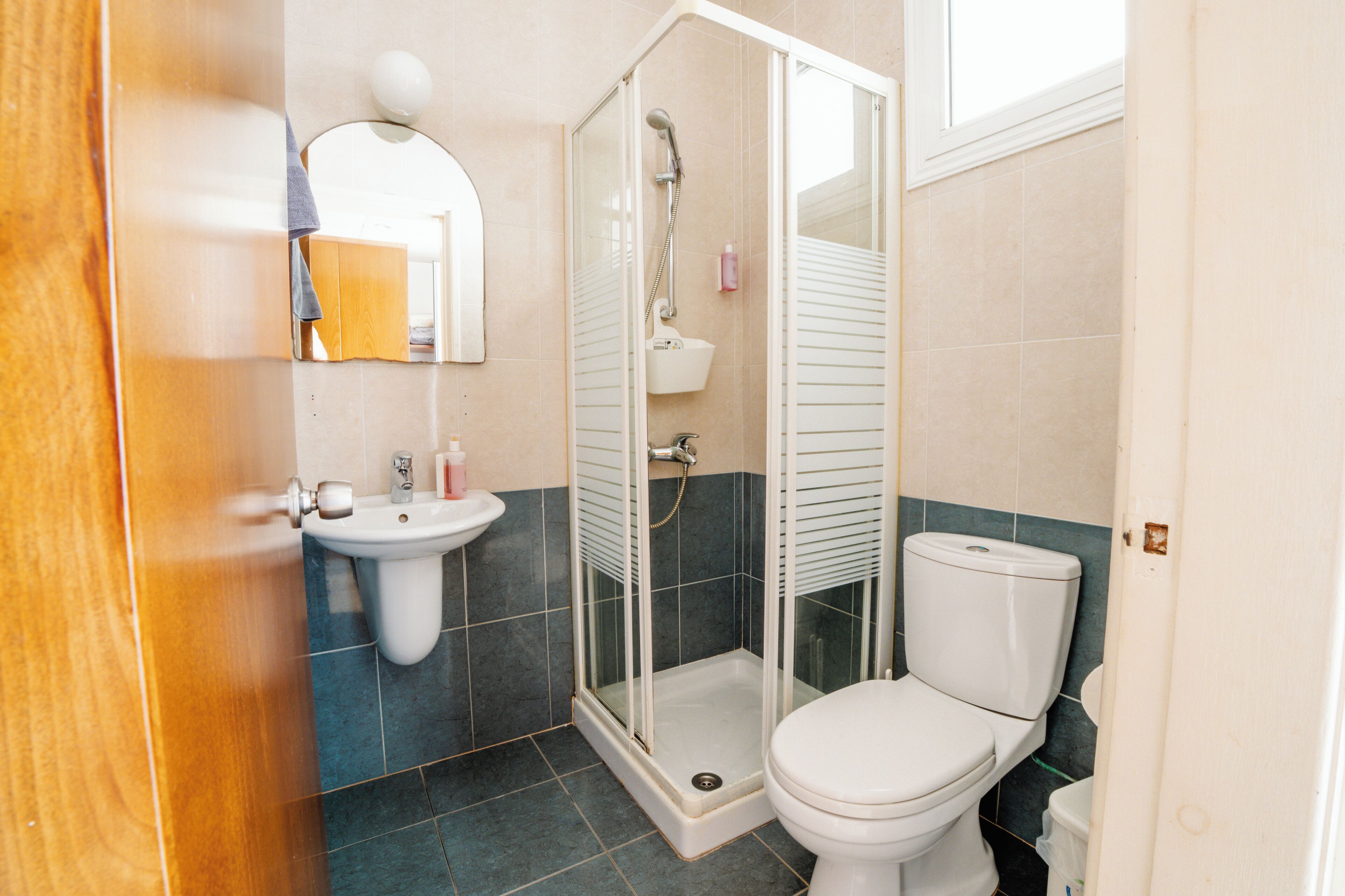 A bathroom with a shower, toilet, sink, and a mirror.