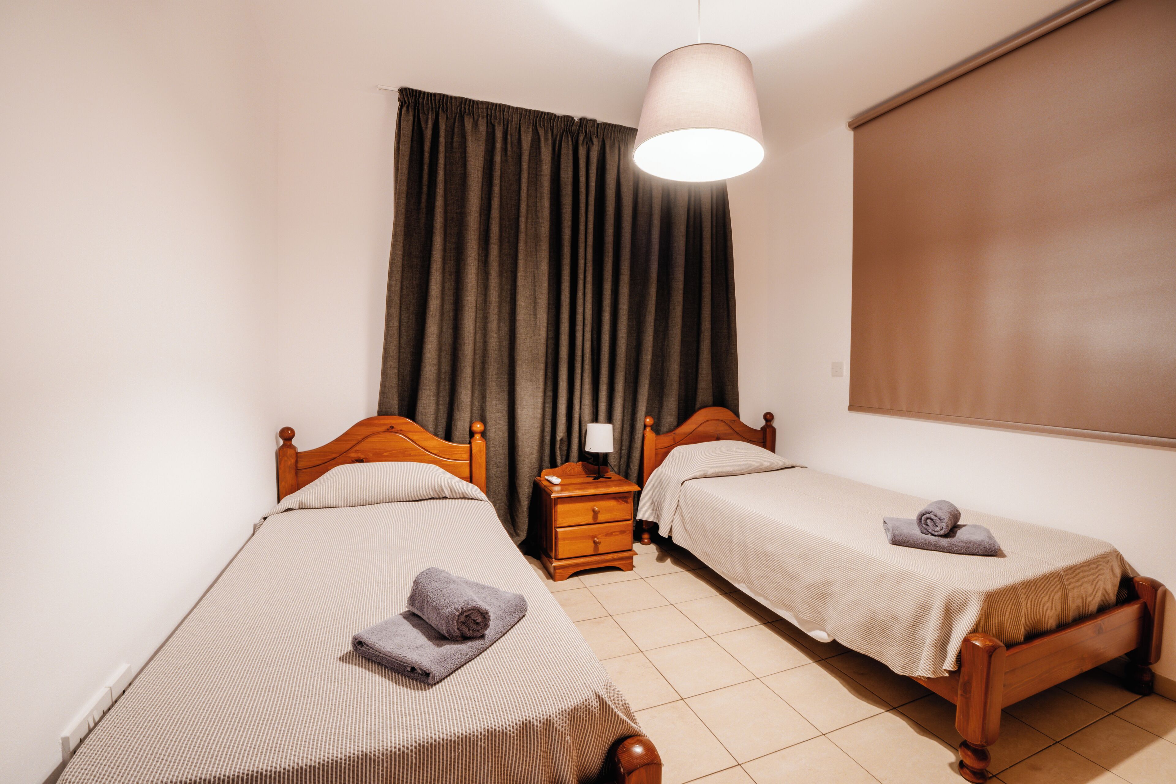 A twin room with two single beds, a nightstand with a lamp, and a window with curtains.