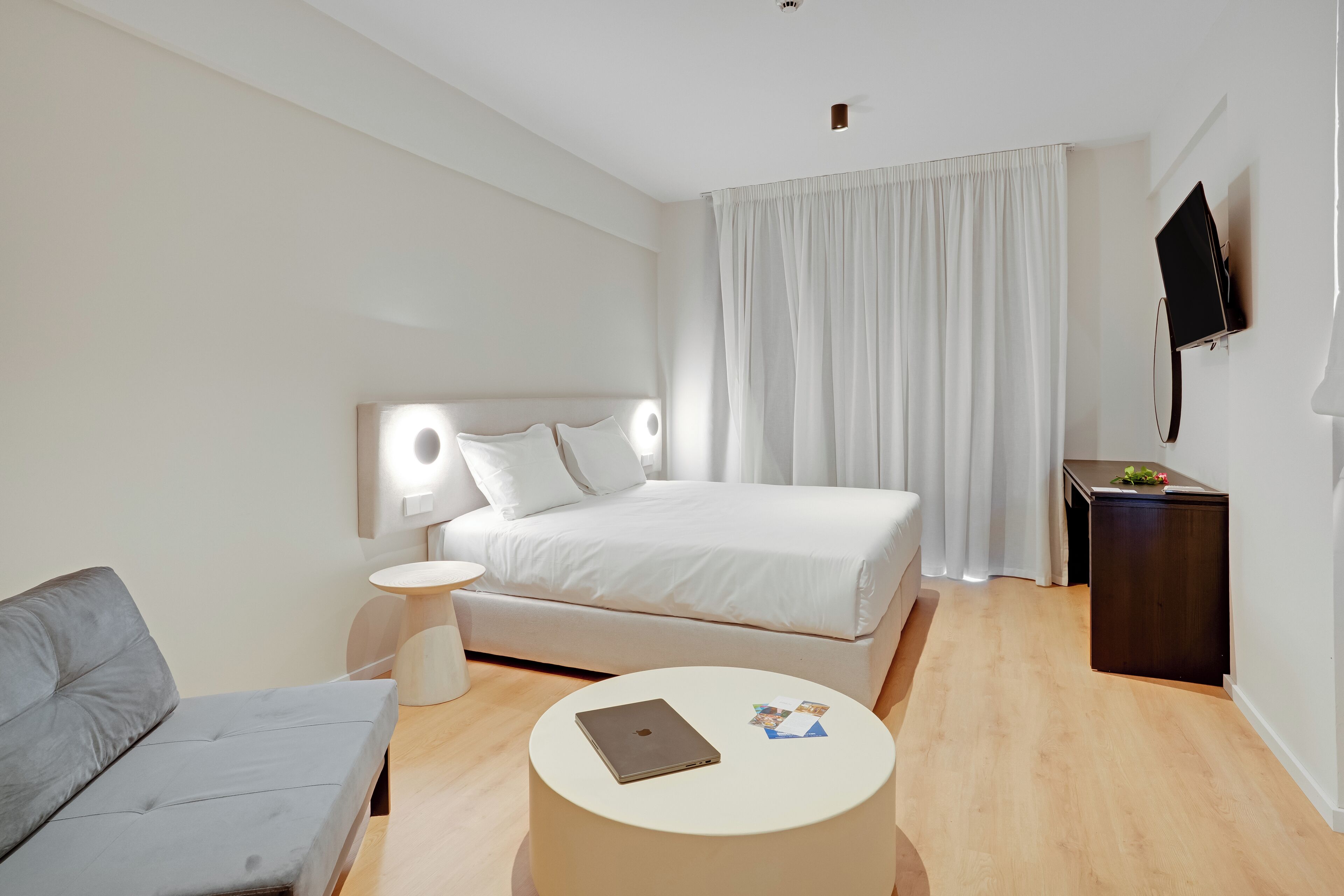 Et moderne hotelværelse med seng, sofa, rundt sofabord, TV og et lille natbord.