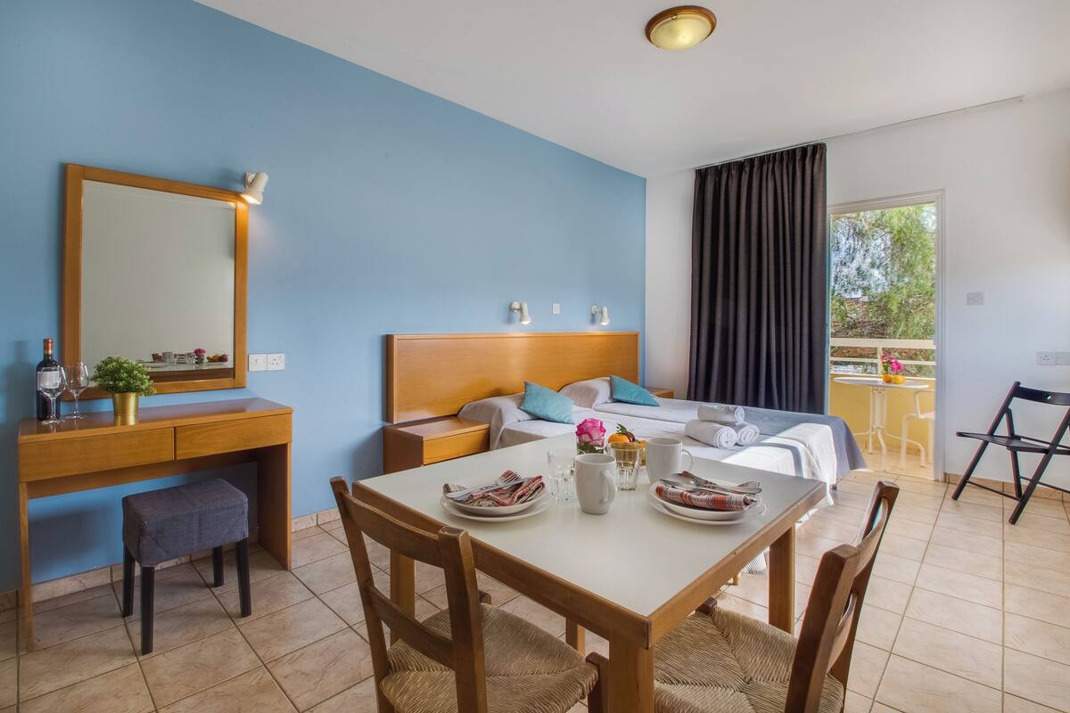 A hotel room with a bed, bedside table, desk, and dining area.