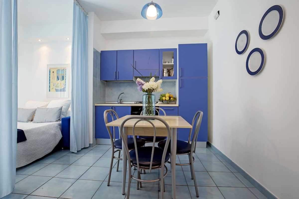 A modern kitchen with blue cabinets, a dining table with four chairs, and a vase with flowers on the table.