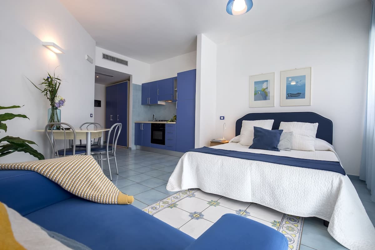 A modern bedroom with a bed, a blue sofa, a dining table, and a kitchen area.