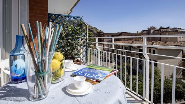 A balcony with a table set for tea, a magazine, and a glass vase with sticks. - Angelina Residence (Maiori)