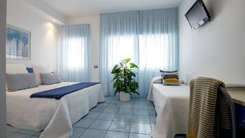 A hotel room with two beds, a desk, a TV, and a potted plant.