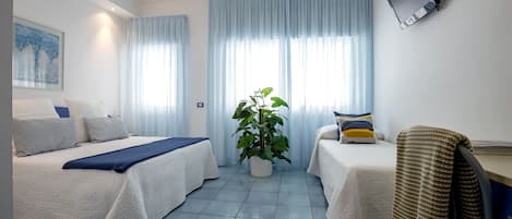 A hotel room with two beds, a desk, a TV, and a potted plant.