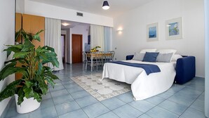 A bedroom with a bed, bedside tables, a potted plant, and a dining area with a table and chairs. - Angelina Residence (Maiori)