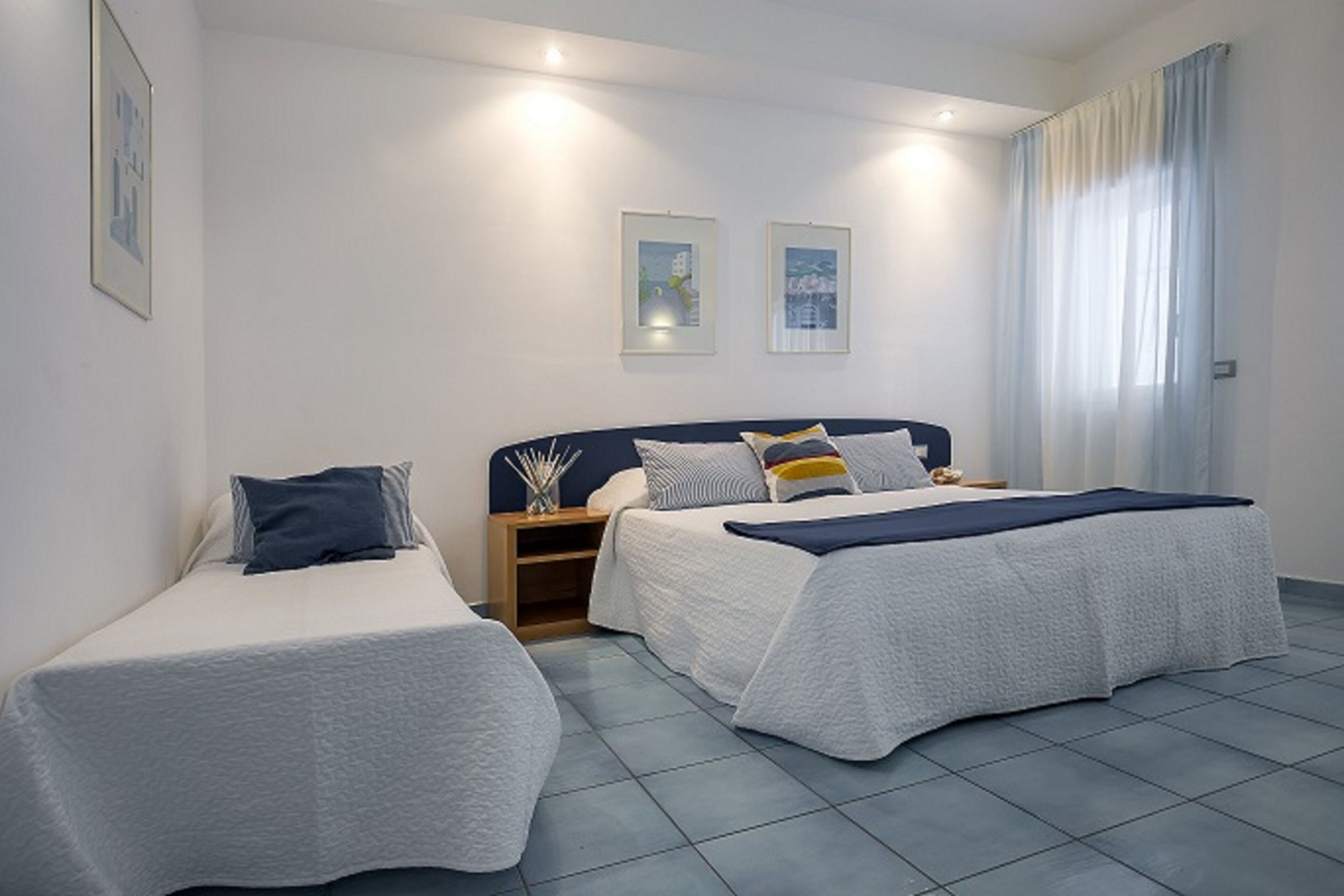A hotel room with two single beds, a nightstand, and a window with curtains.
