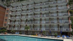 A multi-story hotel with balconies, a swimming pool, and a mountainous backdrop. - Angelina Residence (Maiori)