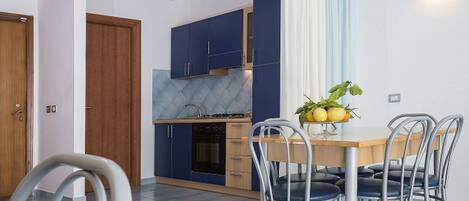 A modern kitchen with blue cabinets, a wooden dining table, and a fruit bowl.