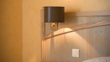 A hotel room with a wooden nightstand, a bedside lamp, and a patterned bedspread.