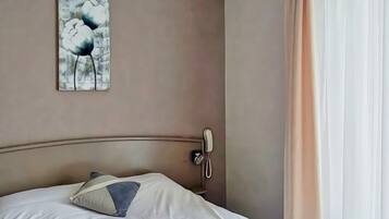 A hotel room with a bed, a painting on the wall, a telephone, and a window with curtains.