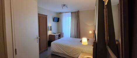 Habitación de hotel con cama, mesita de noche, lámpara, escritorio, silla y televisor en la pared.