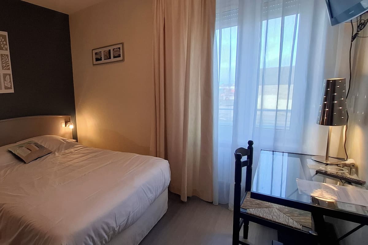 A hotel room with a bed, bedside lamps, a nightstand, a desk with a lamp, and a window with curtains.