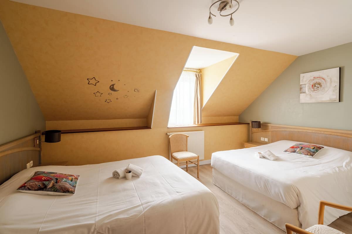 A room with two beds, a chair, a radiator, a window, and a wall with a star and moon design.