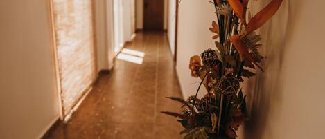 A hallway with a floral arrangement on the right wall, a wooden floor, and a door at the end.