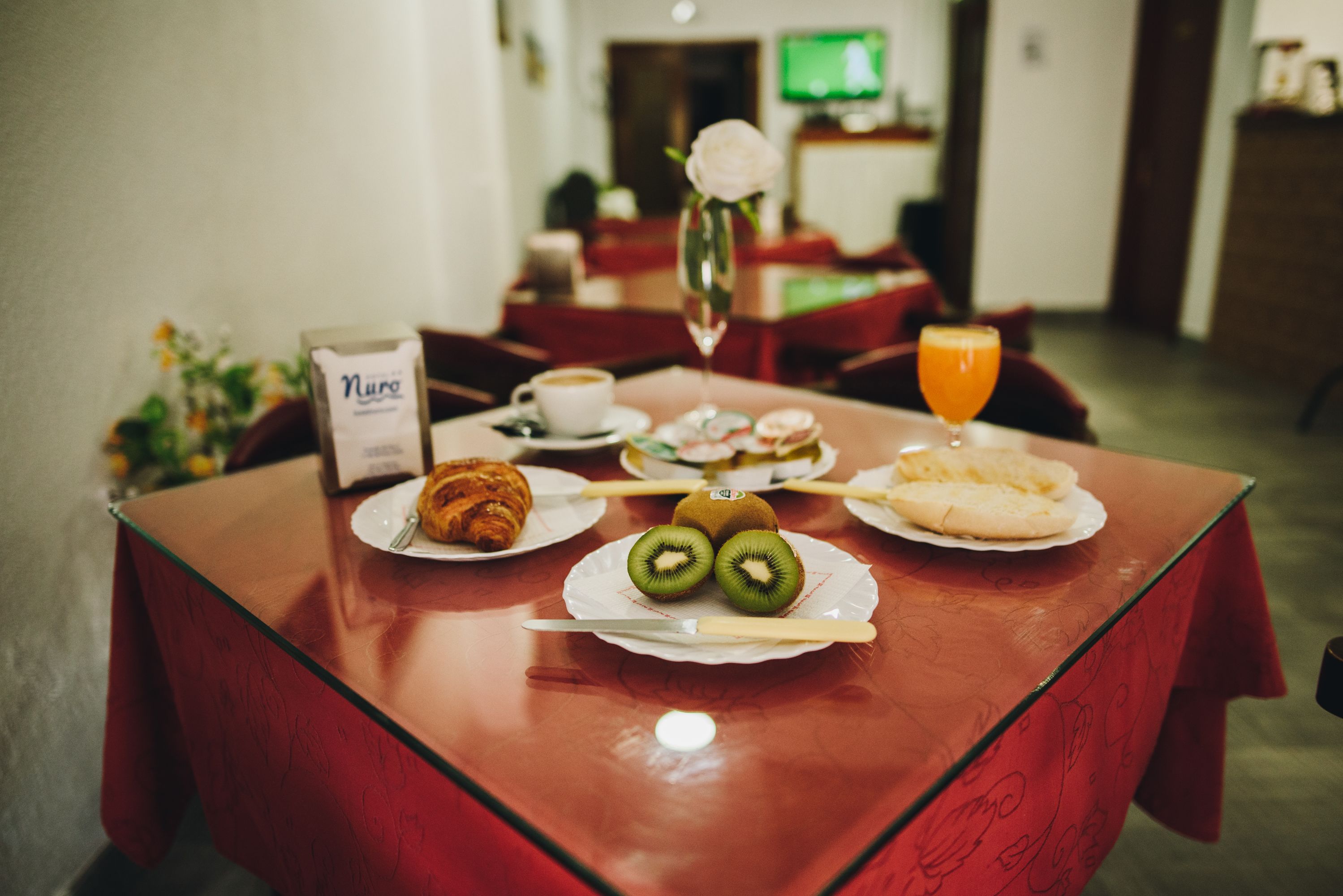 A breakfast table with croissants, kiwi slices, a glass of orange juice, and a coffee cup.