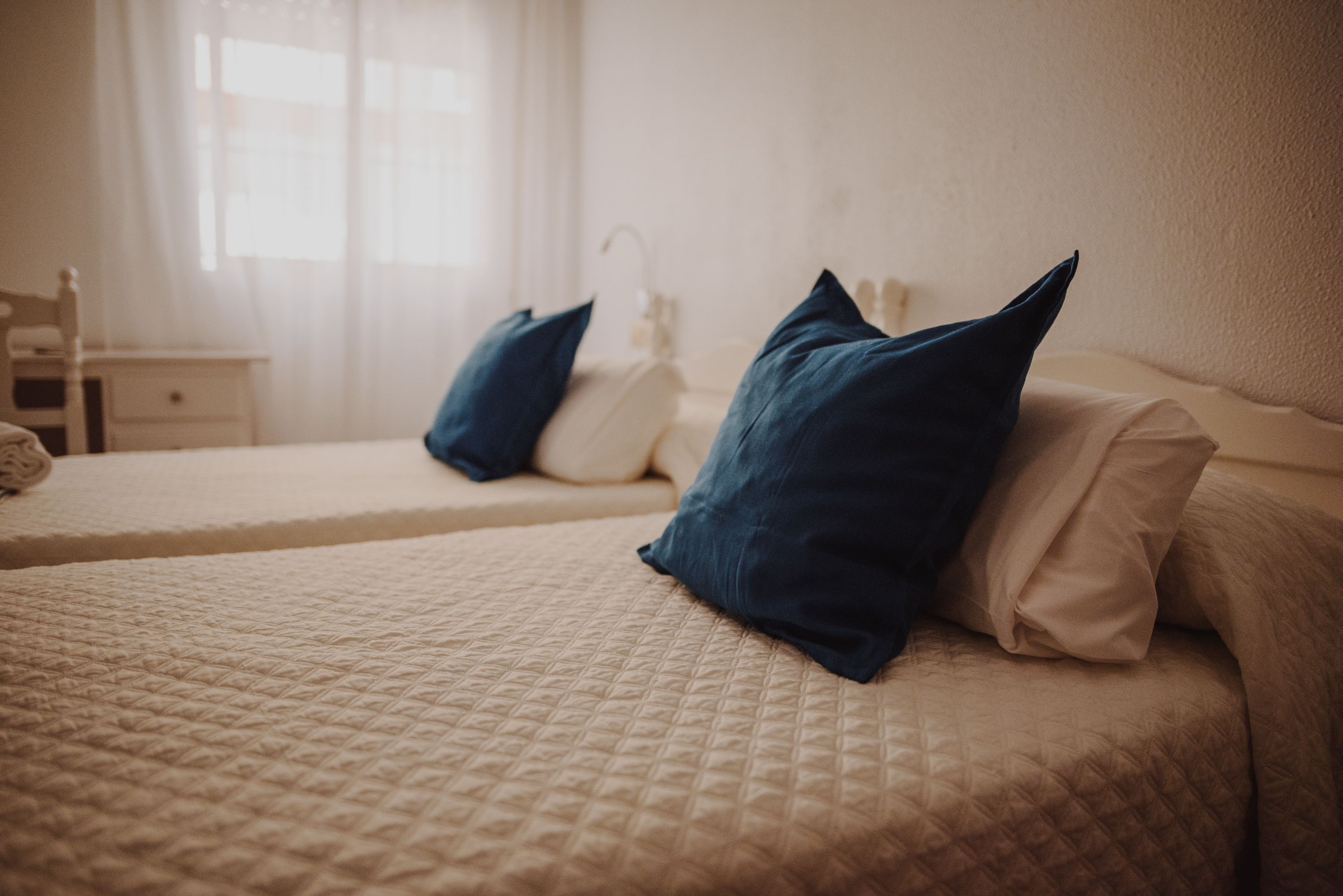 A hotel room with two beds, each with a quilted bedspread and pillows.